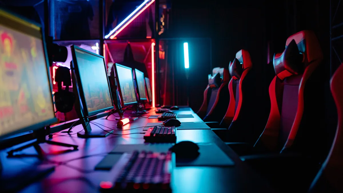 A dimly lit room with multiple computer monitors and gaming chairs, suggesting an esports arena or gaming setup.